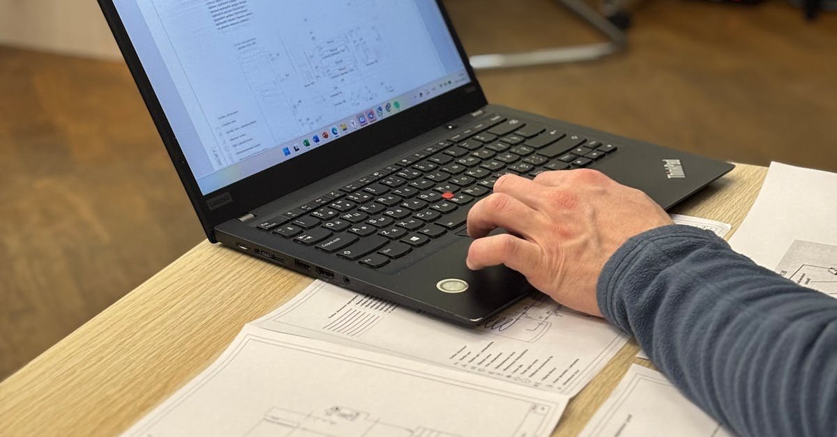 An engineer works on a laptop reviewing technical blueprints and diagrams in an office.